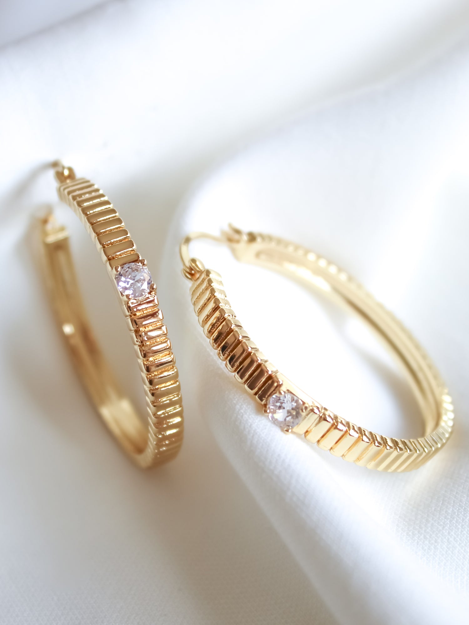 The Quinn Hoop Large by Kinsey Designs Archives features a textured gold filled design with a small clear gemstone, displayed on white fabric—perfect for adding elegance to any look. Shop exclusive sample sale finds now.