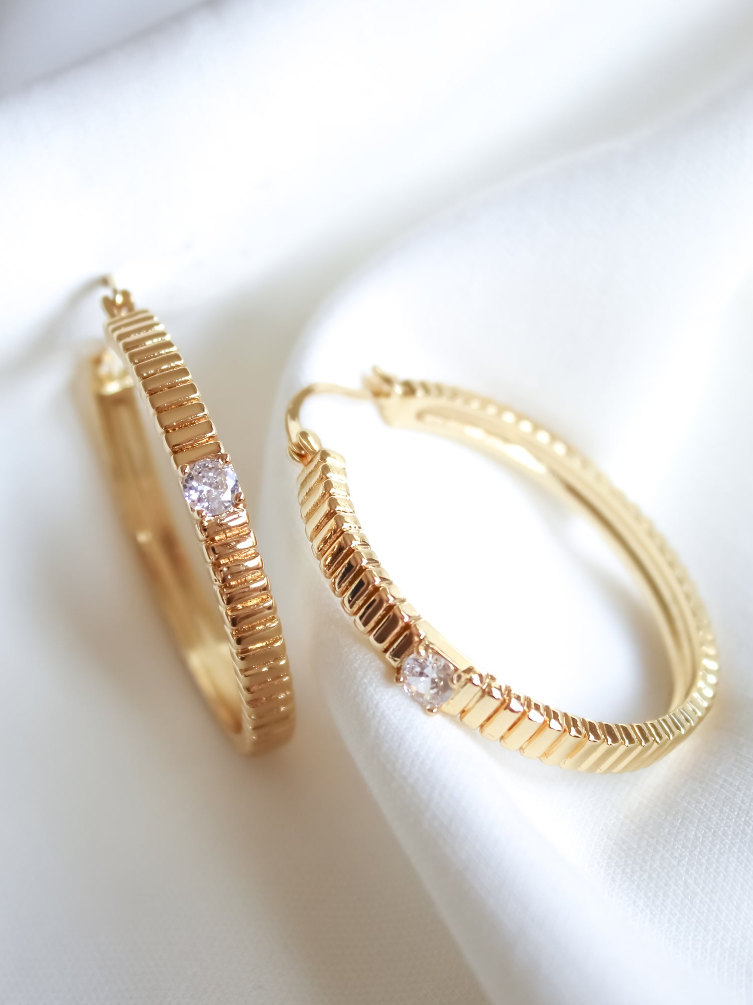 Quinn Hoop Large by Kinsey Designs Archives—gold filled hoops with a textured design and a clear gemstone, displayed on white fabric. Elevate your style with these elegant earrings, now available at our sample sale.