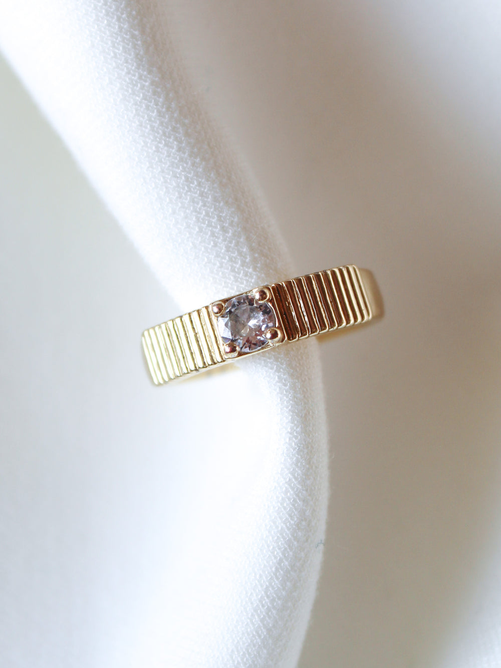 The Quinn Ring by Kinsey Designs is a gold stacking band with a single clear CZ stone, elegantly displayed on white fabric.