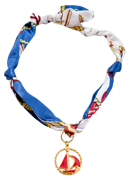 The Rome Scarf Necklace by Kinsey Designs features an adjustable blue and white patterned silk scarf and a gold sailboat pendant charm.