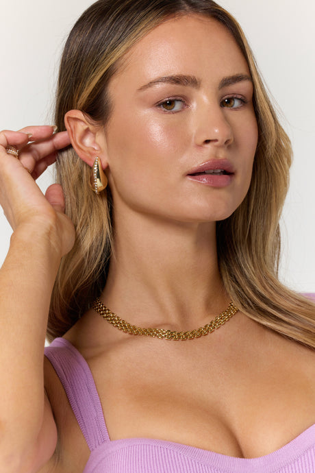 Woman in a lilac top wearing Kinsey Designs' Rhine Teardrop gold filled earrings and a gold chain necklace, looking at the camera.