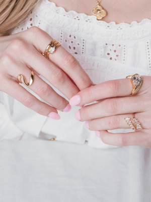 Woman with light pink nails wearing multiple gold rings, including the Kinsey Designs Rowan Coil Ring, and a white eyelet dress.