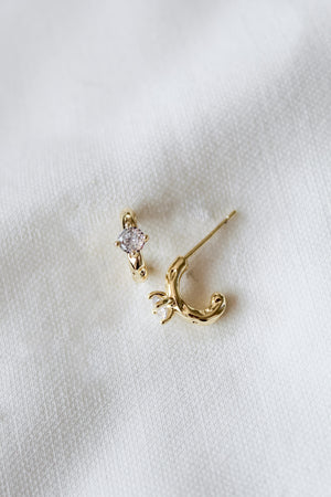 The Kinsey Designs Rugo Hoop and a crescent moon earring rest elegantly on a white textured fabric background.