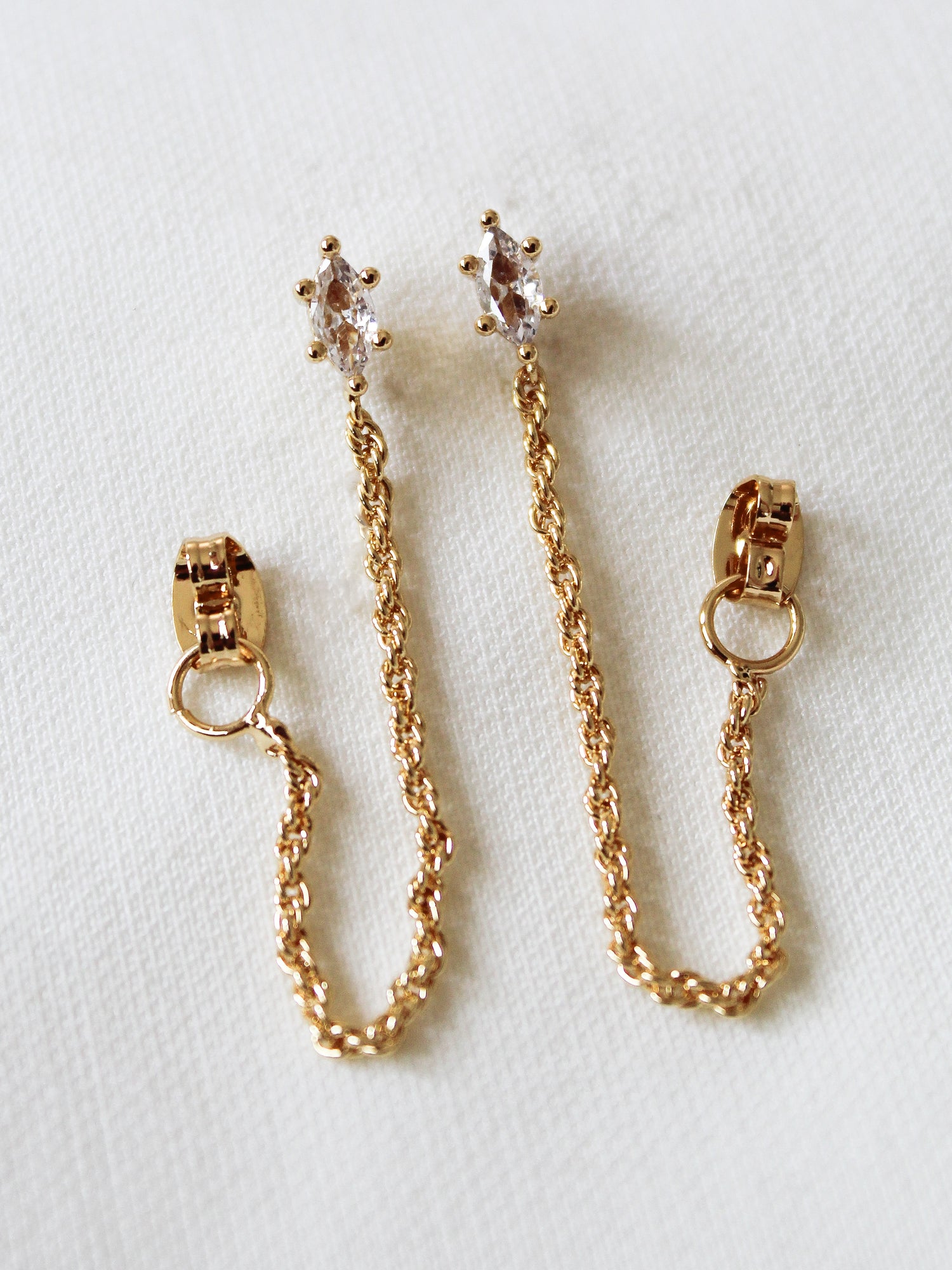 The Kinsey Designs Sadie Wrap Earrings are gold filled, 1.25" long, with clear gemstone studs, displayed on a white fabric background.