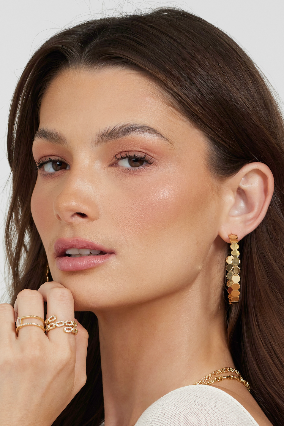 Woman with long brown hair wears gold hoop earrings and the Kinsey Designs Peyton Ring, a gold-plated chain link style, looking at the camera with a neutral expression.
