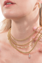 A woman wears the Kinsey Designs Kandi Necklace, a layered gold filled piece, and a gold earring, with her hand gently touching her neck.