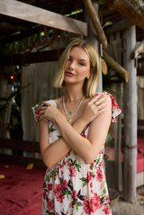 A woman in a floral dress stands outdoors, arms crossed and relaxed, her Kinsey Designs Giselle Pearl Necklace of shimmering freshwater pearls adding elegance to her look.
