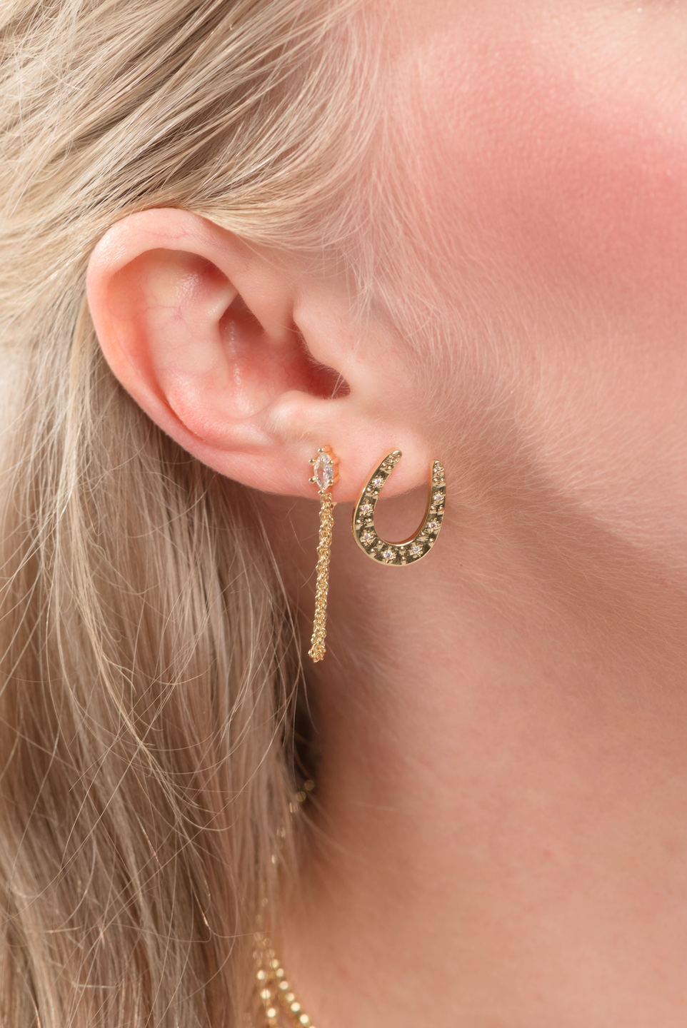 Close-up of a woman's ear wearing the Kent Earring by Kinsey Designs, featuring gold filled horseshoe and chain drop details.