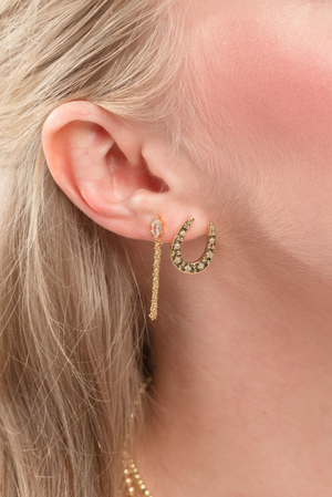 Close-up of a woman's ear wearing the Kent Earring by Kinsey Designs, featuring gold filled horseshoe and chain drop details.