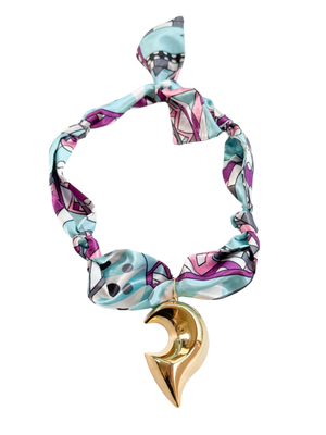 The Prato Scarf Necklace by Kinsey Designs features a colorful patterned fabric and a gold crescent moon pendant, adding unique scarf jewelry style, shown against a white background.