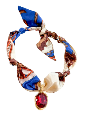 The Umbria Scarf Necklace by Kinsey Designs features colorful patterns and a vintage pendant with a red gemstone. Its adjustable design ensures a perfect fit and adds vibrant style to any look.