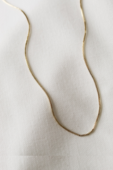 A delicate Kinsey Charm Bar Necklace with a gold-filled bar and box chain is displayed on a white textured fabric, highlighting its adjustable chain for the perfect fit.