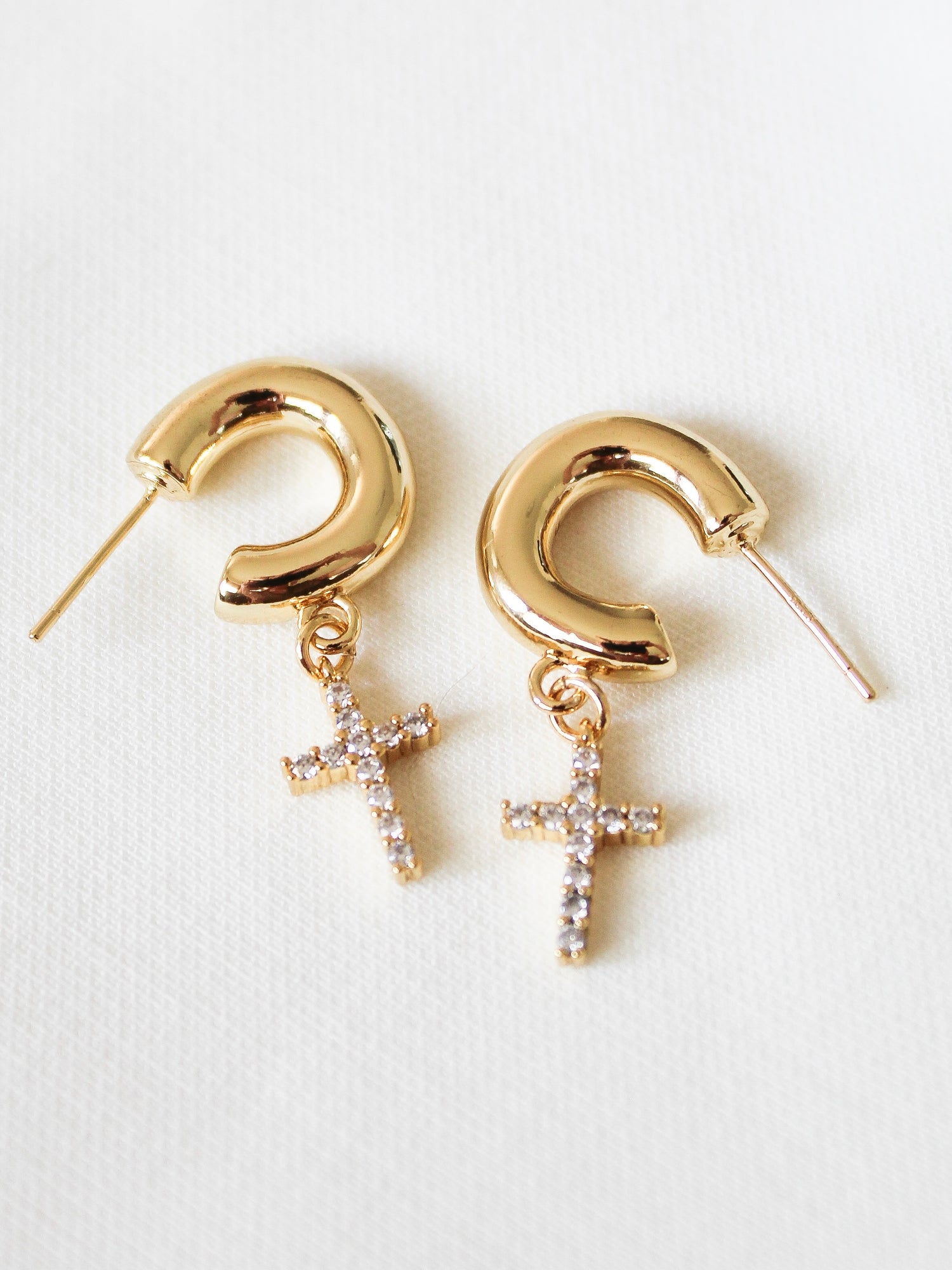The Victoria Hoop by Kinsey Designs Archives features gold-filled hoops with small jeweled cross pendants (1.5" long), displayed on a white fabric background—ideal for adding elegance at our sample sale.