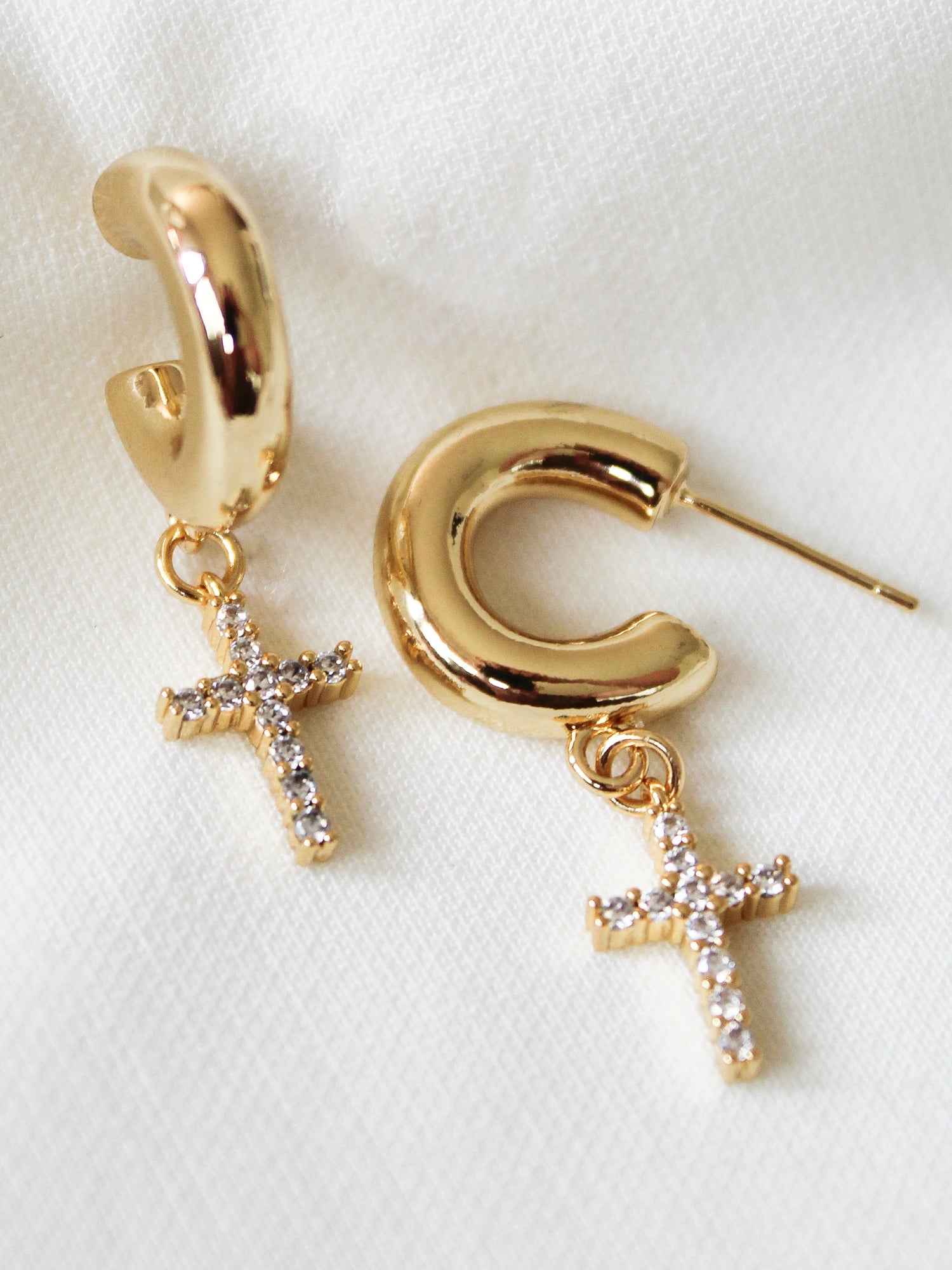 The Victoria Hoop by Kinsey Designs Archives: 1.5" gold filled hoops with sparkling cross pendants, displayed on white fabric. Elevate your style—shop this chic sample sale now!.
