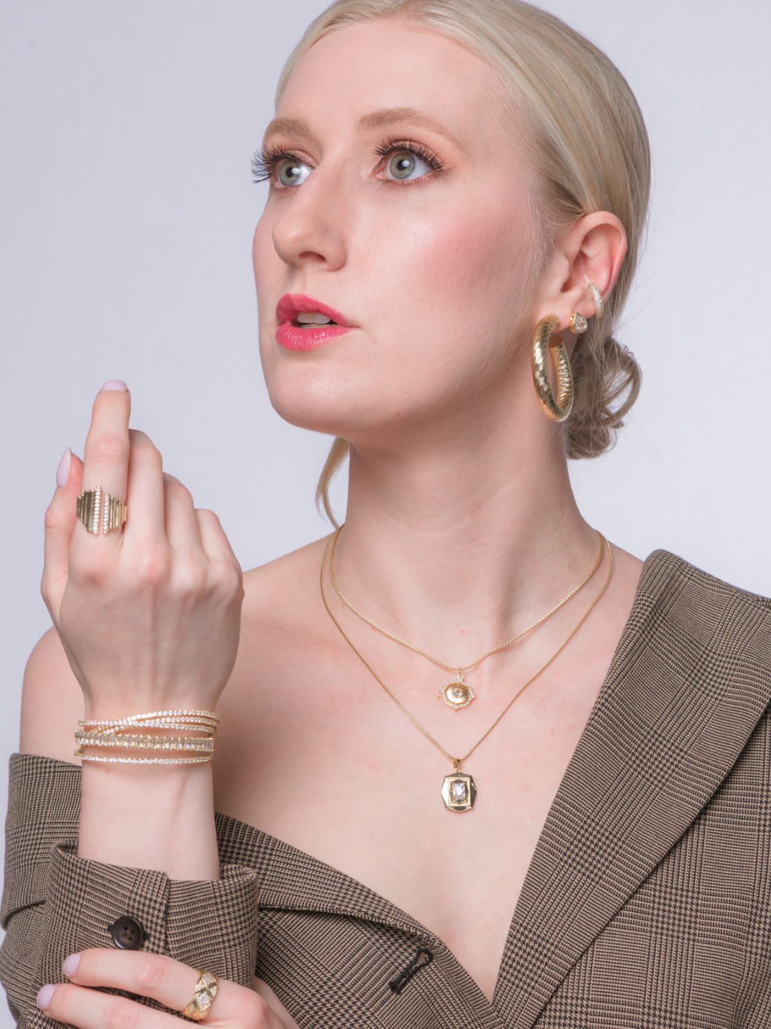A woman in a brown plaid blazer wears the Kinsey Designs Archives Zara Cuff Bracelet, an adjustable gold filled jewelry piece, while gazing upward with a thoughtful expression.