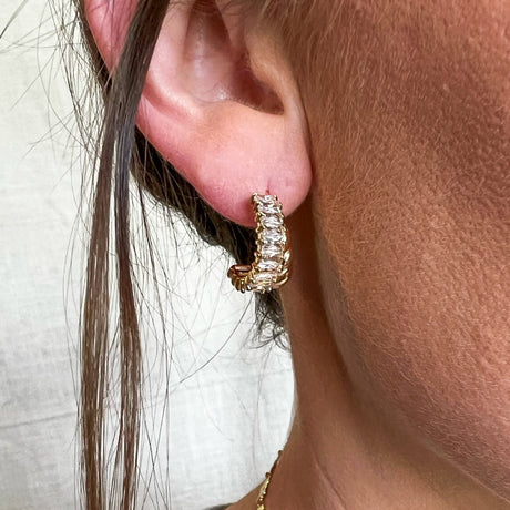 Close-up of a person wearing the Zuri Hoop by Kinsey Designs, featuring gold filled hoops adorned with clear cubic zirconia gemstones along the outer edge.