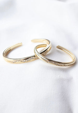Two Lily Cuff bangles by Kinsey Designs Archives, gold filled with a wavy design and embedded cubic zirconia, displayed on white fabric.