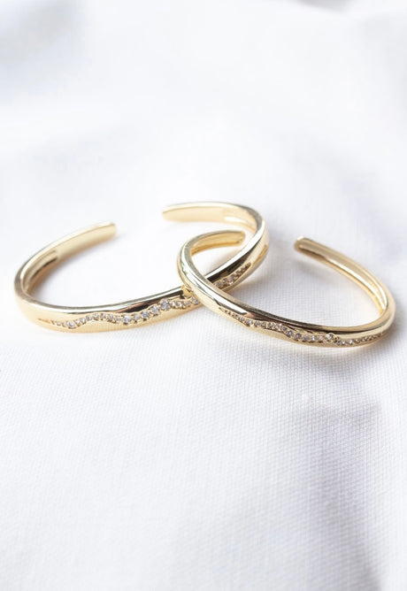 Two Lily Cuff bangles by Kinsey Designs Archives, gold filled with a wavy design and embedded cubic zirconia, displayed on white fabric.