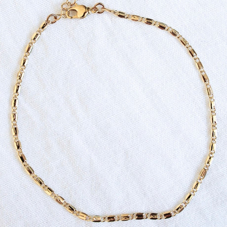 The Hali Anklet by Kinsey Designs Archives features a gold plated chain and lobster clasp, shown on a white textured fabric background.
