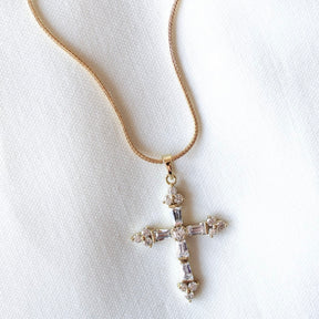 The Jamie Necklace by Kinsey Designs Archives features a gold filled 18" chain and a sparkling cubic zirconia cross pendant, displayed on a white fabric background.