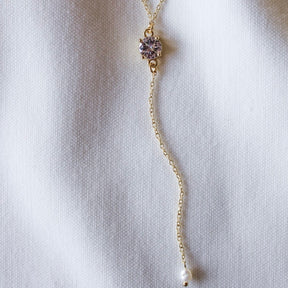 The Logan Lariat by Kinsey Designs Archives is a gold filled necklace with a gemstone, small pearl, and cubic zirconia accent, shown on a white textured fabric background.