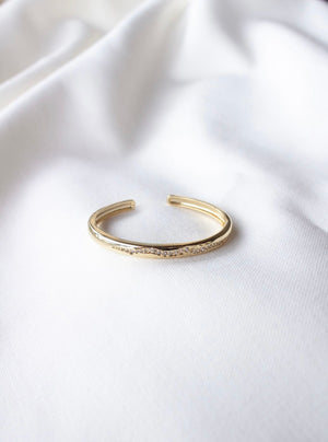 The Lily Baby Cuff by Kinsey Designs, a gold-filled bracelet with small diamonds, rests on a white fabric background—showcasing the elegance of adjustable jewelry.