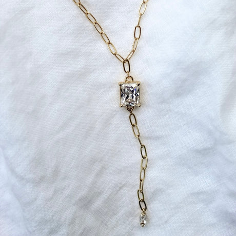The Yara Lariat by Kinsey Designs Archives features a gold filled chain and square cubic zirconia pendant, shown on a white fabric background.