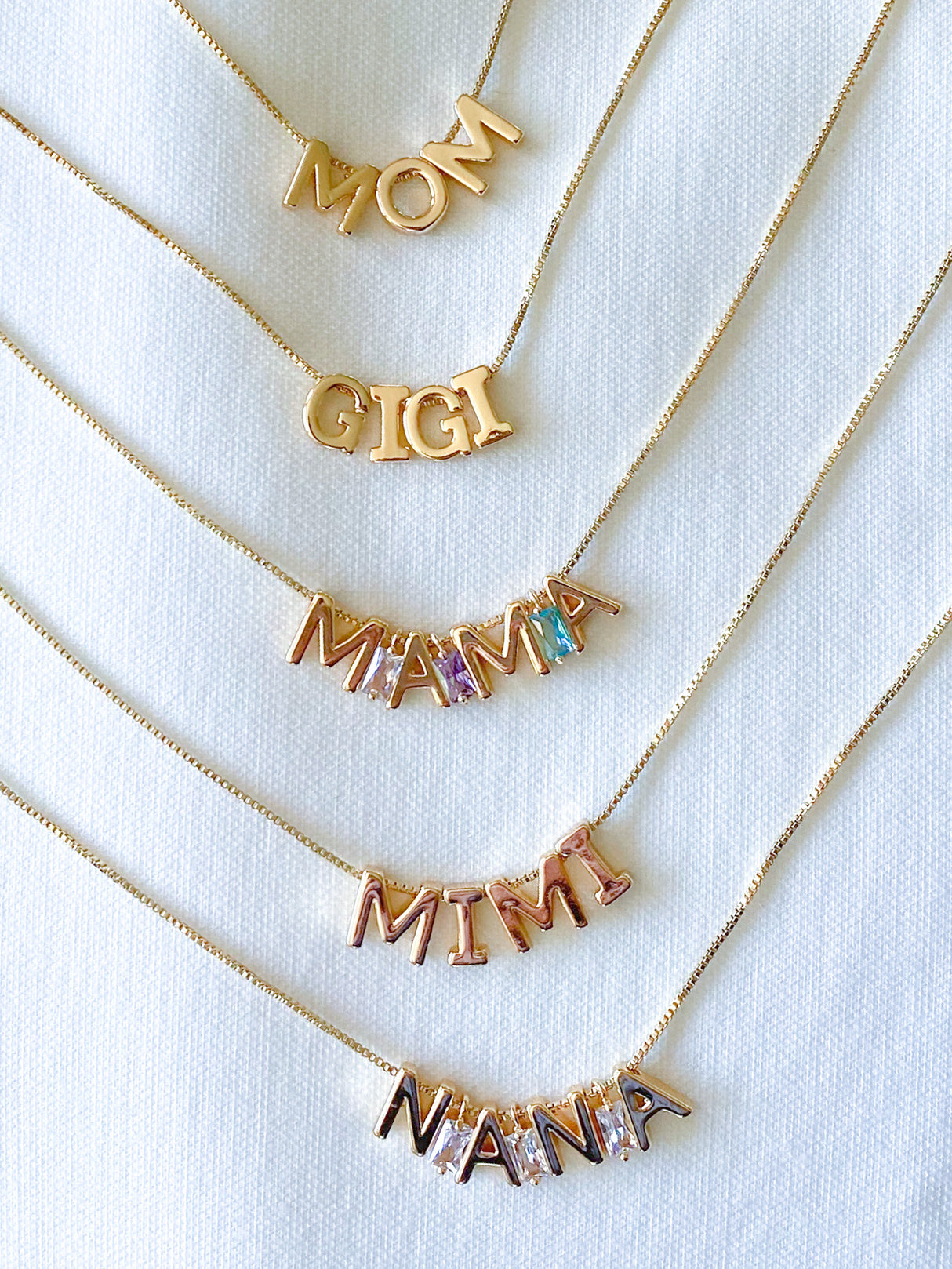 Six adjustable Charm Bar Necklace Box Chain - Kinsey Charm Bar necklaces with pendant letters spelling "MOM," "GIGI," "MAMA," "MIMI," and "NANA" on a white background.