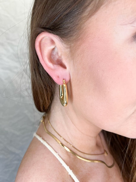 A woman wears the Kepri Hoop by Kinsey Designs Archives—1-inch long gold plated hoops—with layered gold necklaces, shown from the side against a light background. Jewelry measurements available upon request.