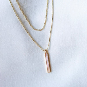 The Kalani Pearl Necklace by Kinsey Designs Archives, featuring a delicate gold-filled chain and a mother-of-pearl vertical rectangular pendant, is displayed on white fabric.