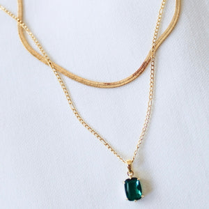 The Kelley Layer by Kinsey Designs Archives features an 18" gold plated chain with a green gemstone pendant, showcased on a white fabric background.