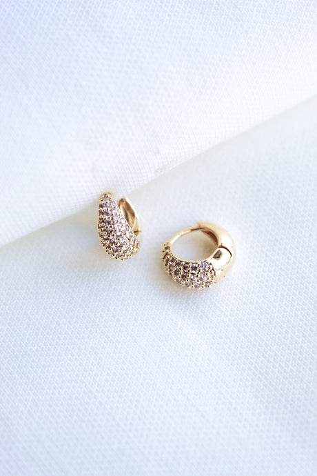 The Beeba Huggie by Kinsey Designs Archives features gold plated hoops with sparkling cubic zirconia stones, measuring 0.5 inch, showcased on a white textured fabric background.