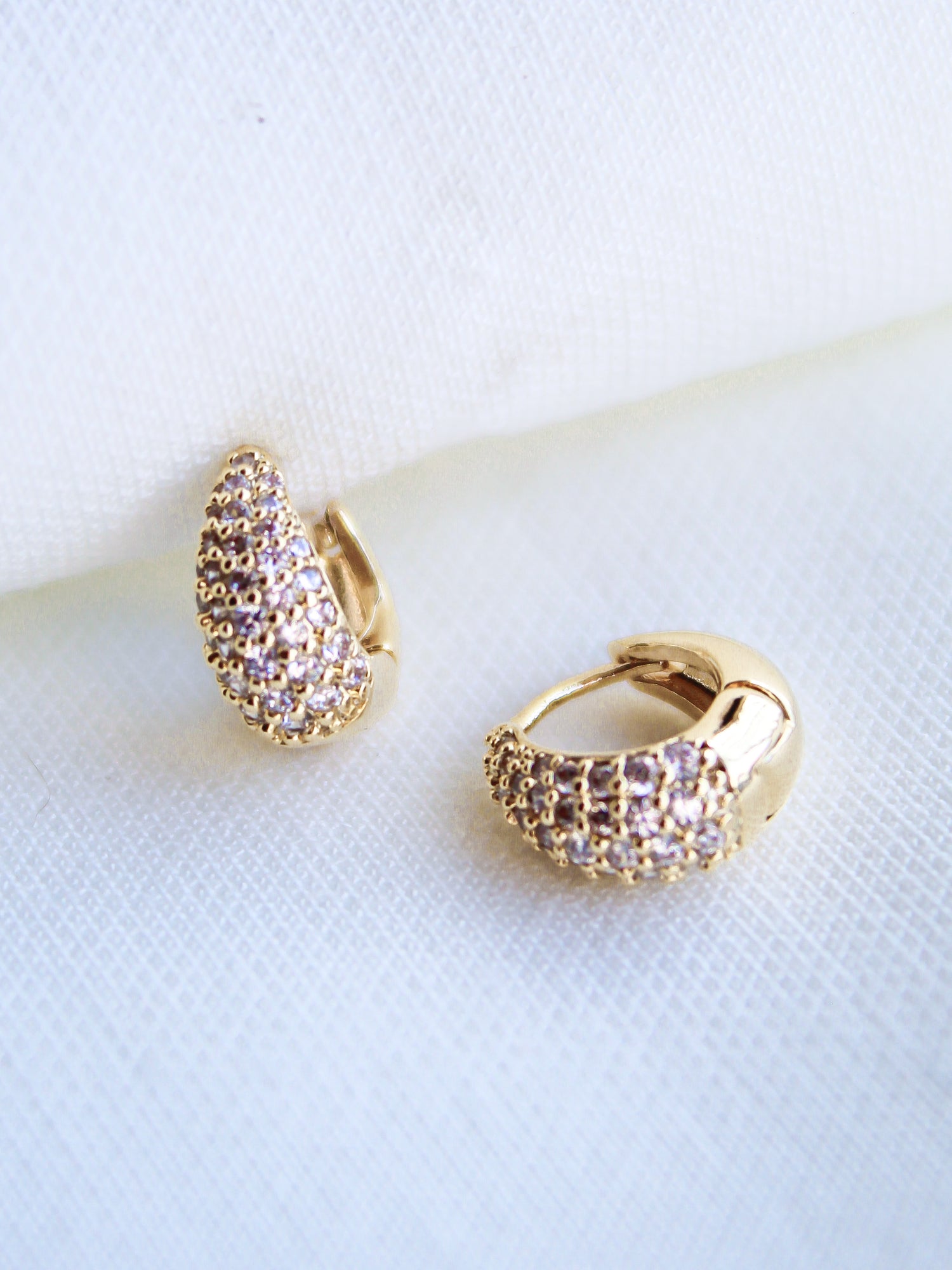 The Beeba Huggie earrings by Kinsey Designs Archives feature sparkling cubic zirconia and gold plating, measuring 0.5 inches, displayed on a white fabric background.