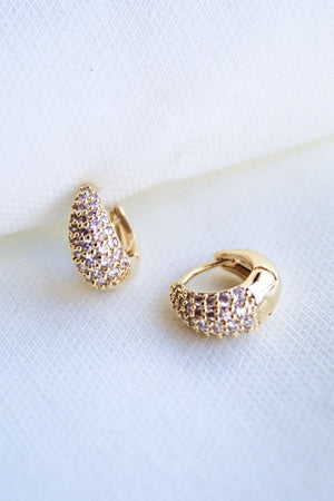 The Beeba Huggie earrings by Kinsey Designs Archives feature sparkling cubic zirconia and gold plating, measuring 0.5 inches, displayed on a white fabric background.
