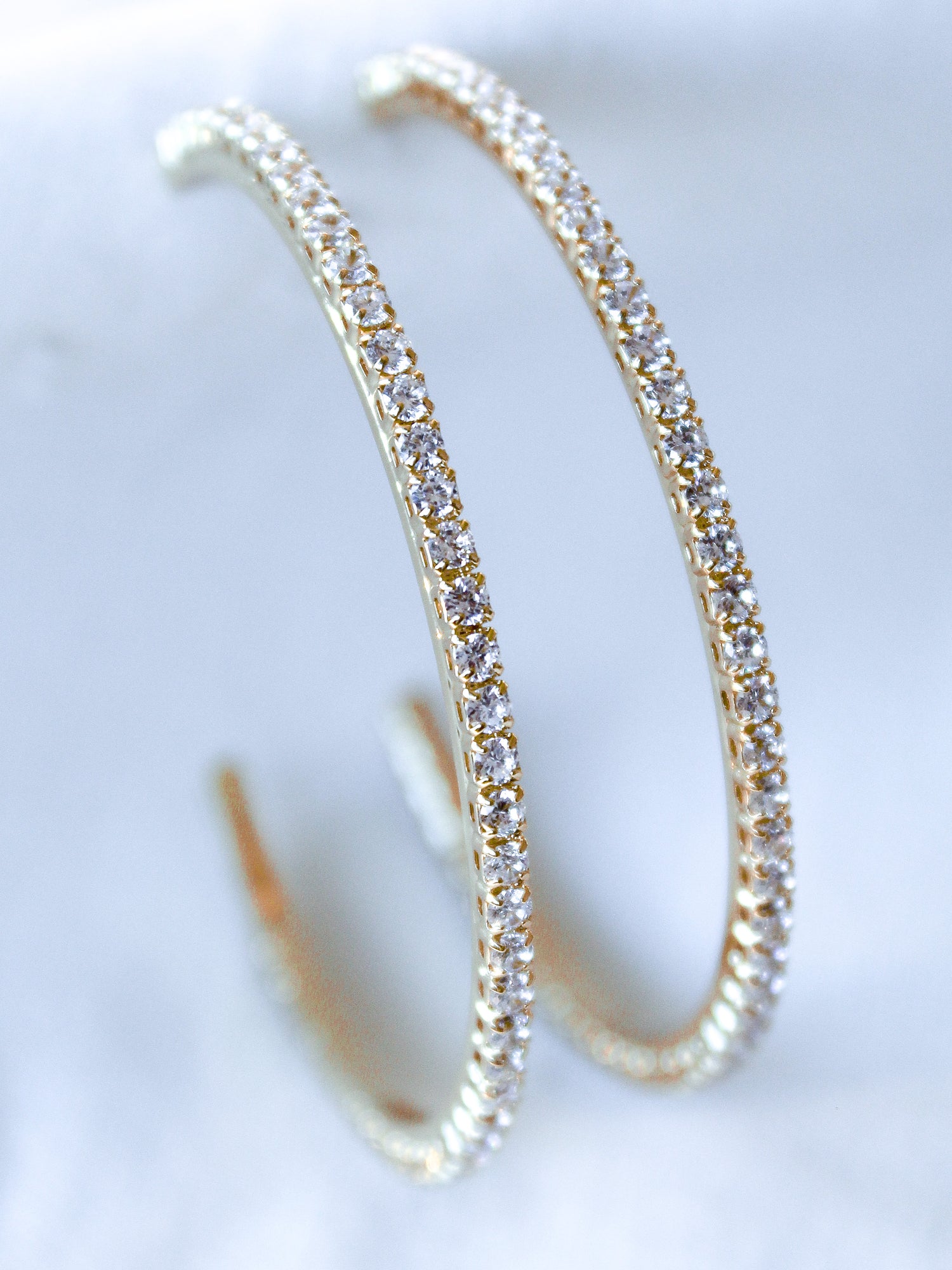 The Blaze Hoop by Kinsey Designs Archives features gold-filled hoops adorned with small cubic zirconia stones, showcased on a soft white surface.