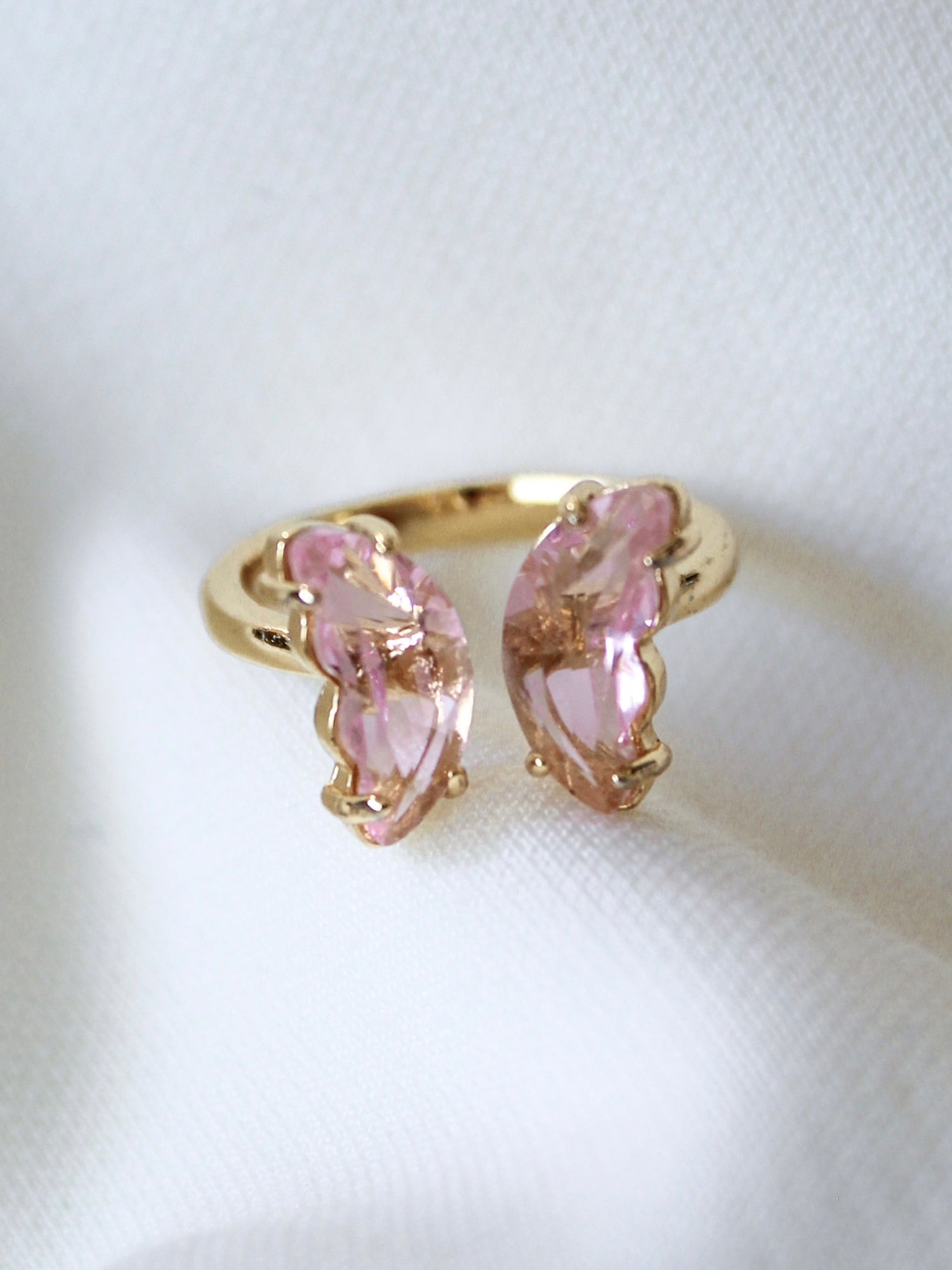 The Bliss Ring - Blush by Kinsey Designs Archives is an adjustable gold plated ring featuring two pink, leaf-shaped stones, shown on a white fabric background.