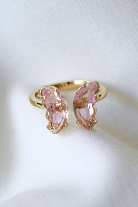 The Bliss Ring - Blush by Kinsey Designs Archives is an adjustable gold plated ring featuring two pink, leaf-shaped stones, shown on a white fabric background.