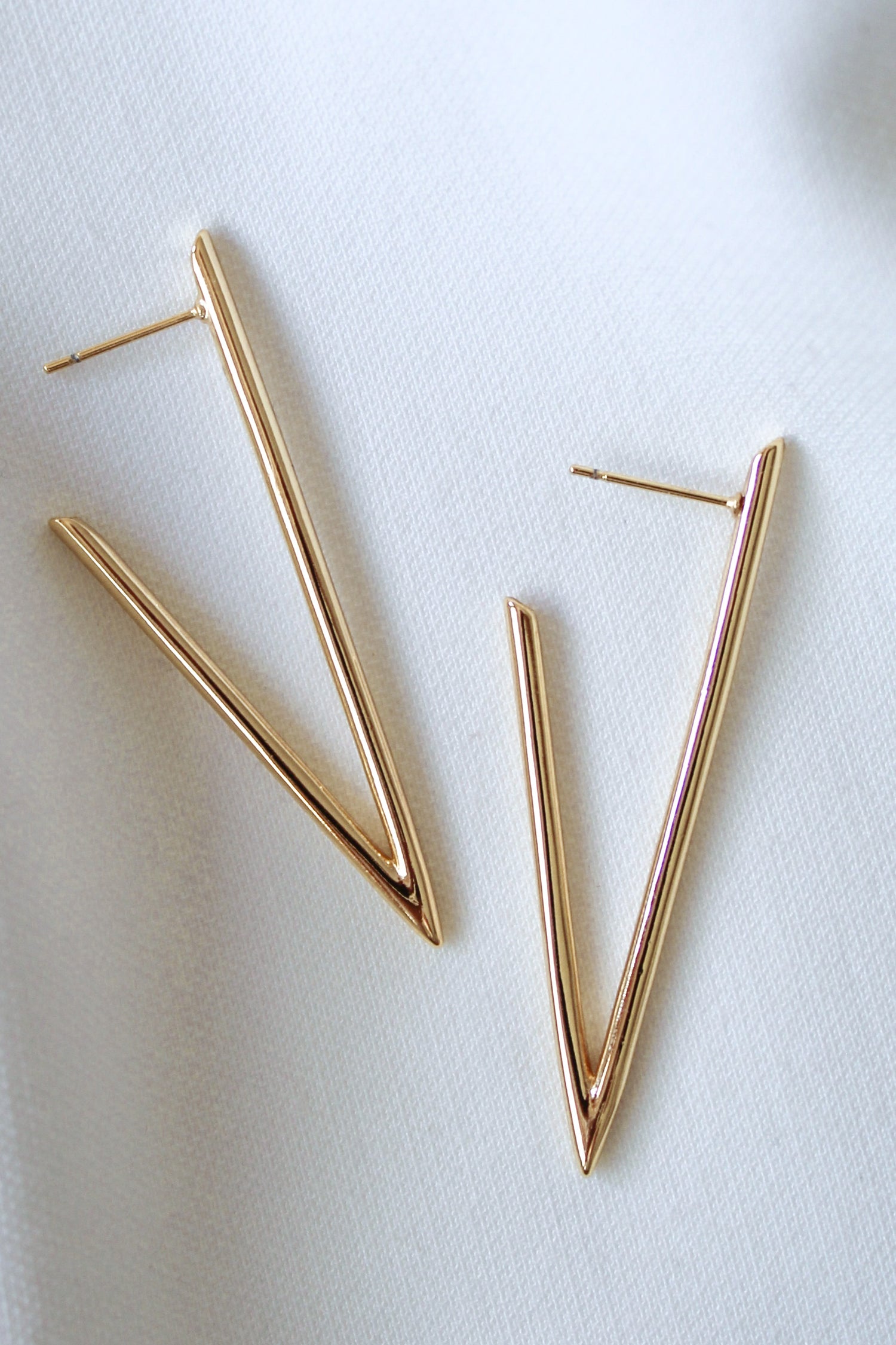 The Bowen Earring by Kinsey Designs features a gold-filled V shape, displayed on white fabric. Elevate your style with these elegant earrings—shop now during our exclusive sample sale!.
