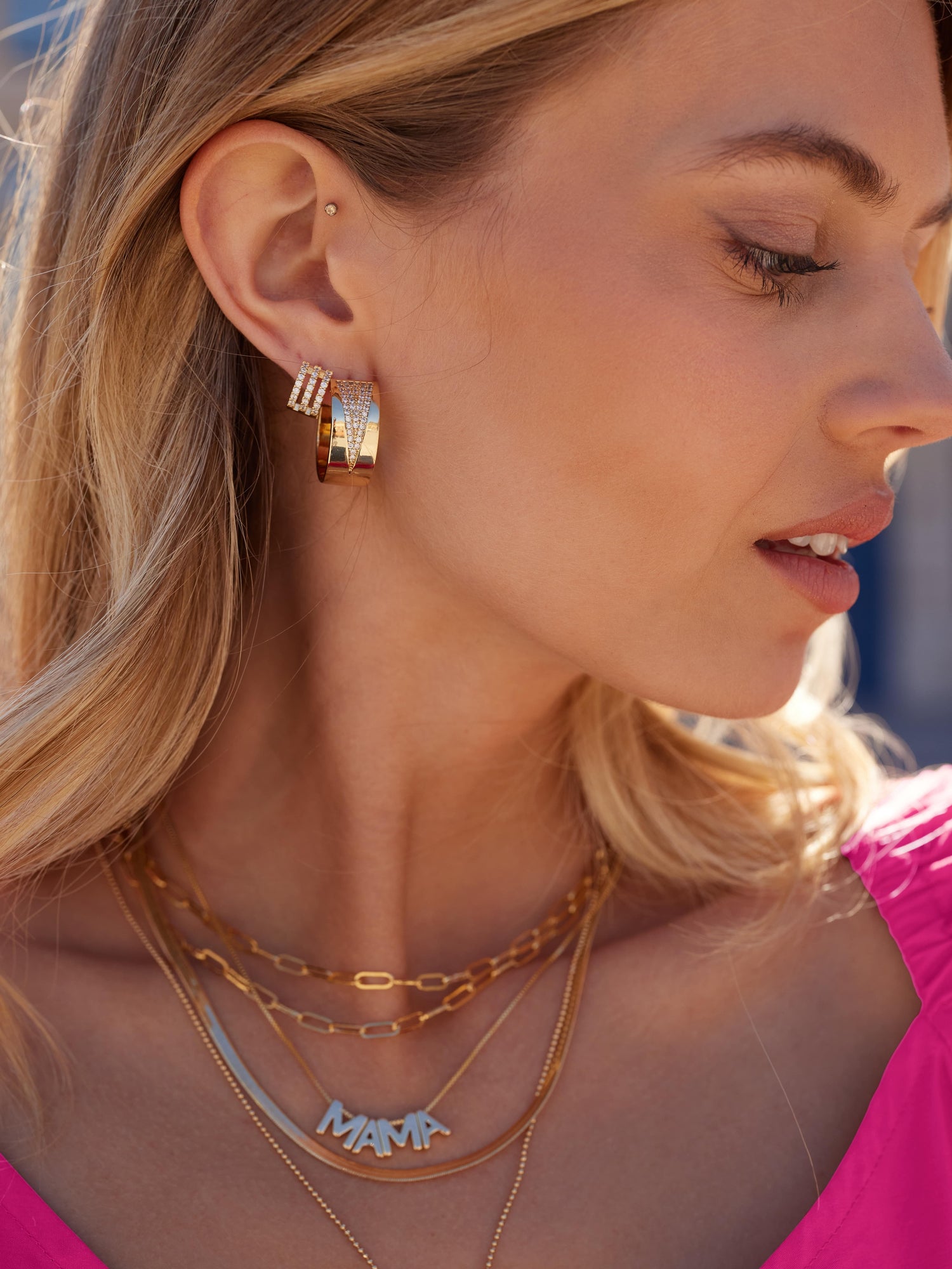A woman in a pink top is shown in profile wearing Kinsey Designs Archives' Bri Huggie 14k gold plated earrings and layered gold necklaces.