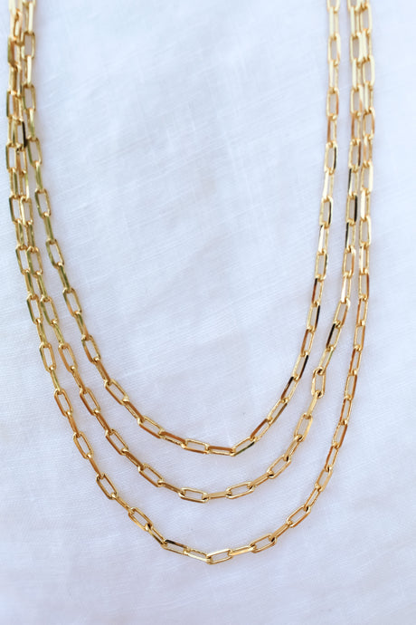 The Kinsey Designs Archives Carmen Triple Layer features three gold-filled chain necklaces with rectangular links and an adjustable extender, shown on a white fabric background.