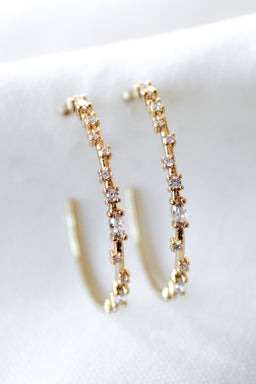 The Chase Hoop Large earrings by Kinsey Designs, gold filled and embellished with sparkling gemstones, are displayed on a white fabric background.