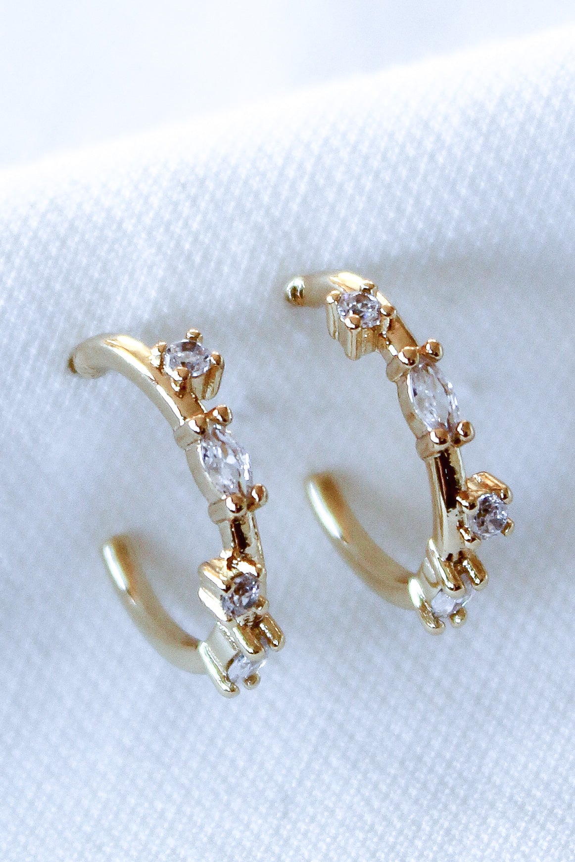 The Kinsey Designs Chase Hoop Mini features gold-filled hoops with sparkling cubic zirconia stones set along the top. These 0.5" diameter earrings offer a delicate, elegant touch, shown on a white fabric background.