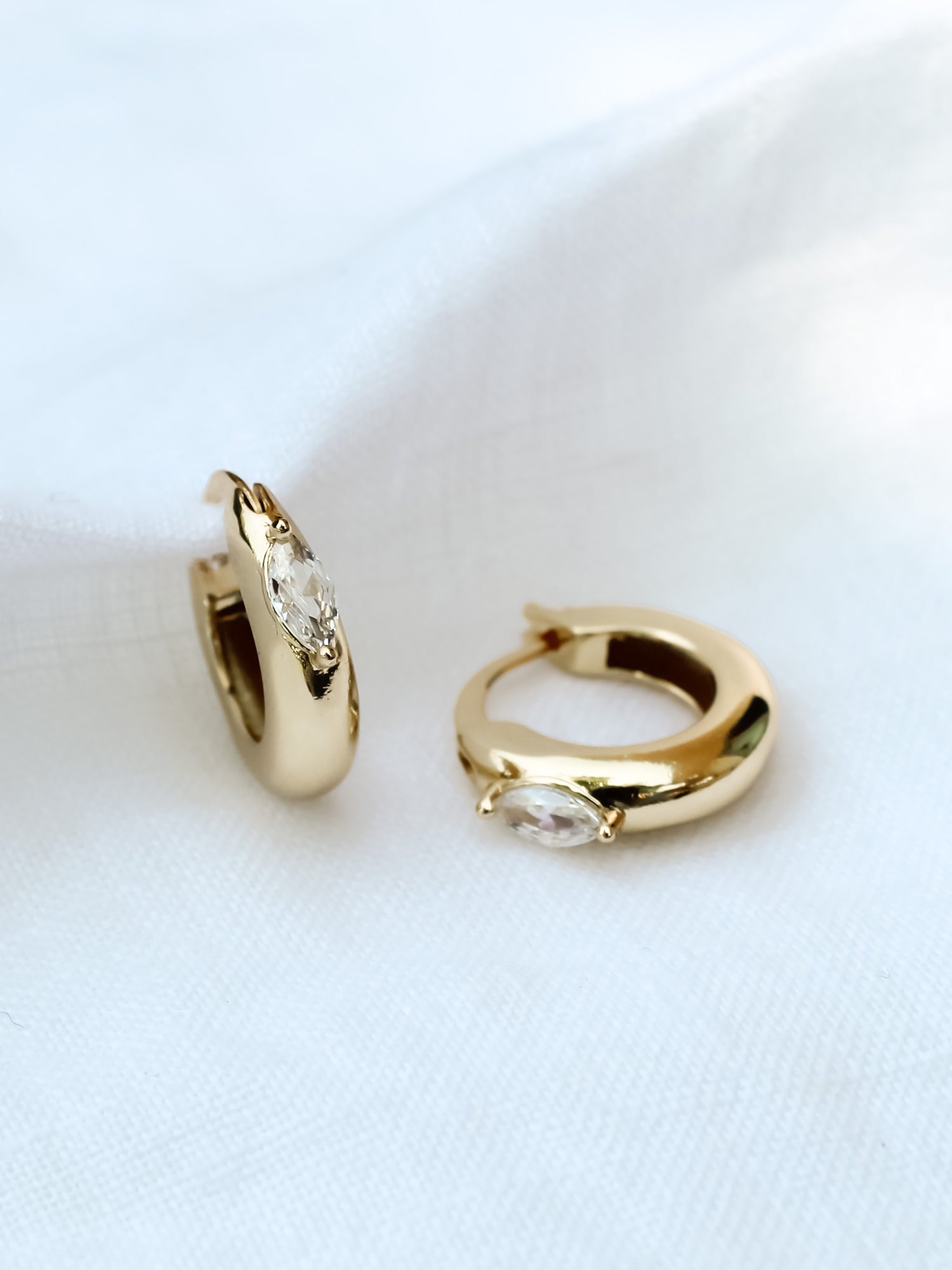 The Claudia Huggie by Kinsey Designs Archives features two gold-filled hoop earrings with marquise-cut cubic zirconia stones (.75" circumference), shown on a white fabric background.