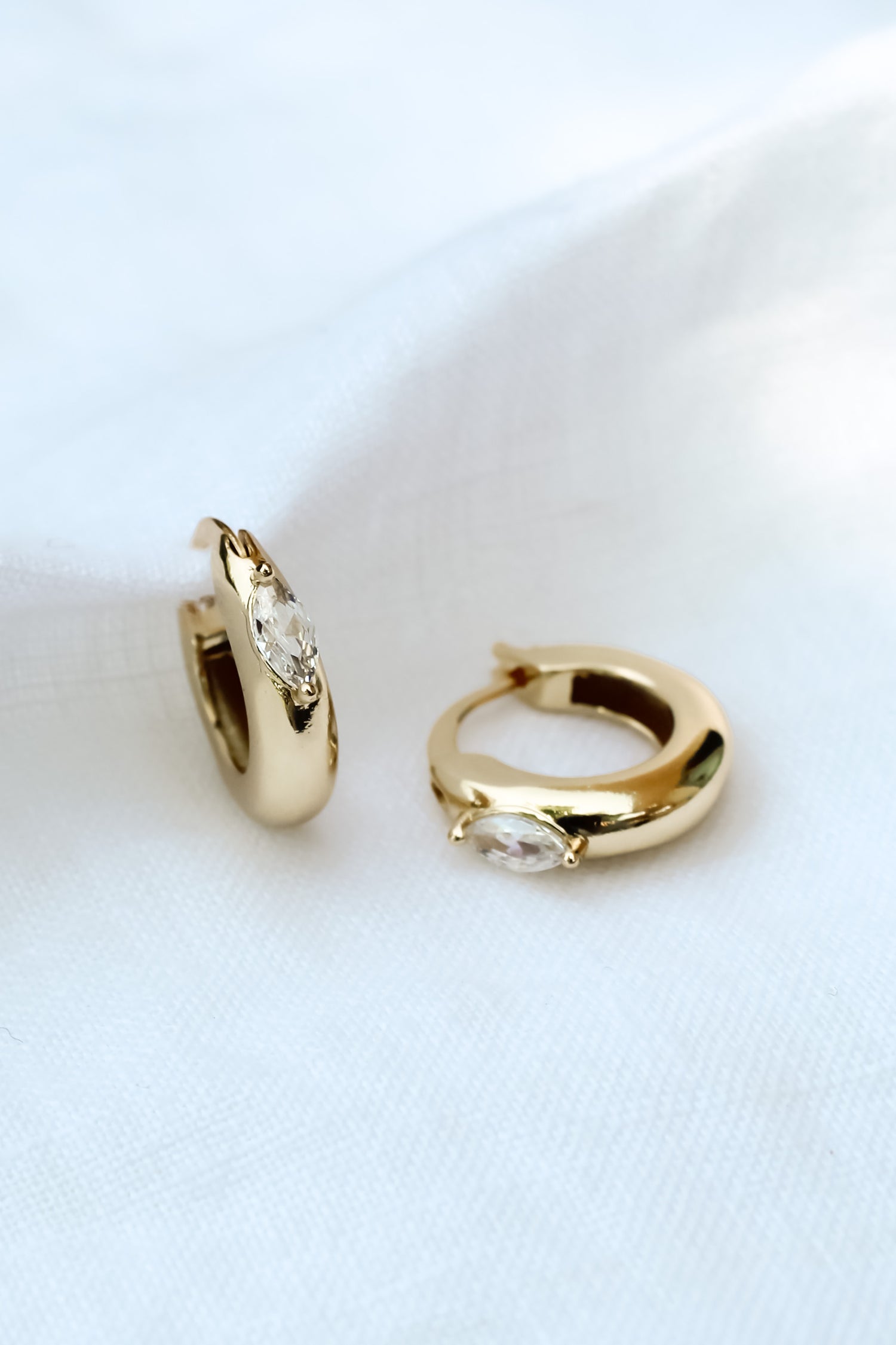 The Claudia Huggie by Kinsey Designs Archives features two gold-filled hoop earrings with marquise-cut cubic zirconia stones (.75" circumference), shown on a white fabric background.