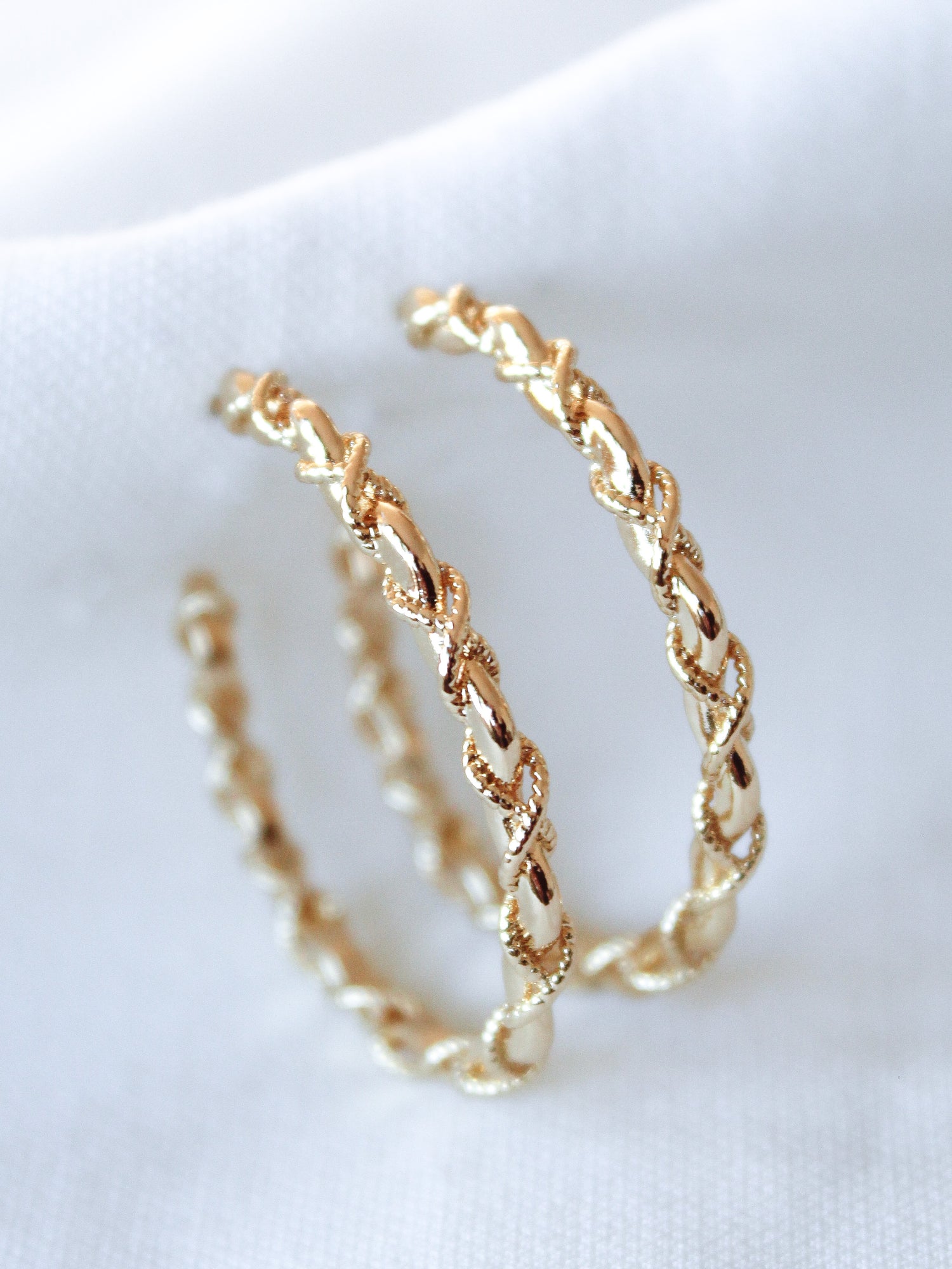 The Cru Hoop by Kinsey Designs Archives features two gold filled hoops with a twisted, chain-like design and 1.25" diameter, shown on a white fabric background.