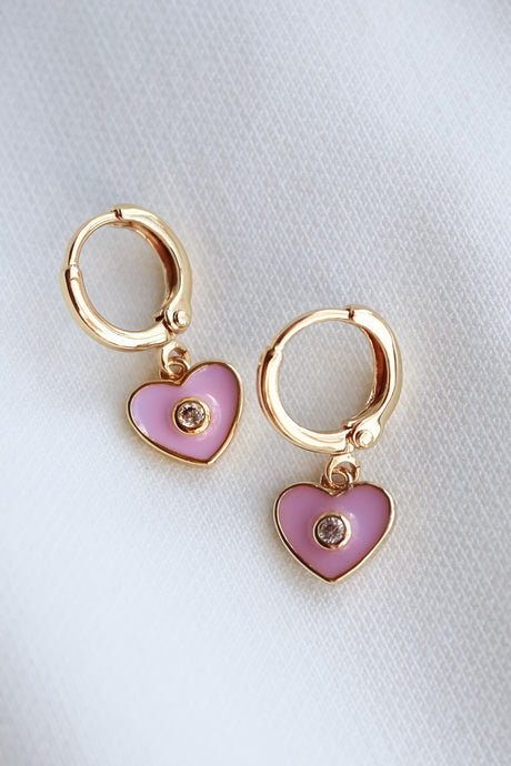 The Cutie Huggie by Kinsey Designs Archives: 1-inch gold-filled earrings with pink heart-shaped charms and a central gemstone, displayed on white fabric.