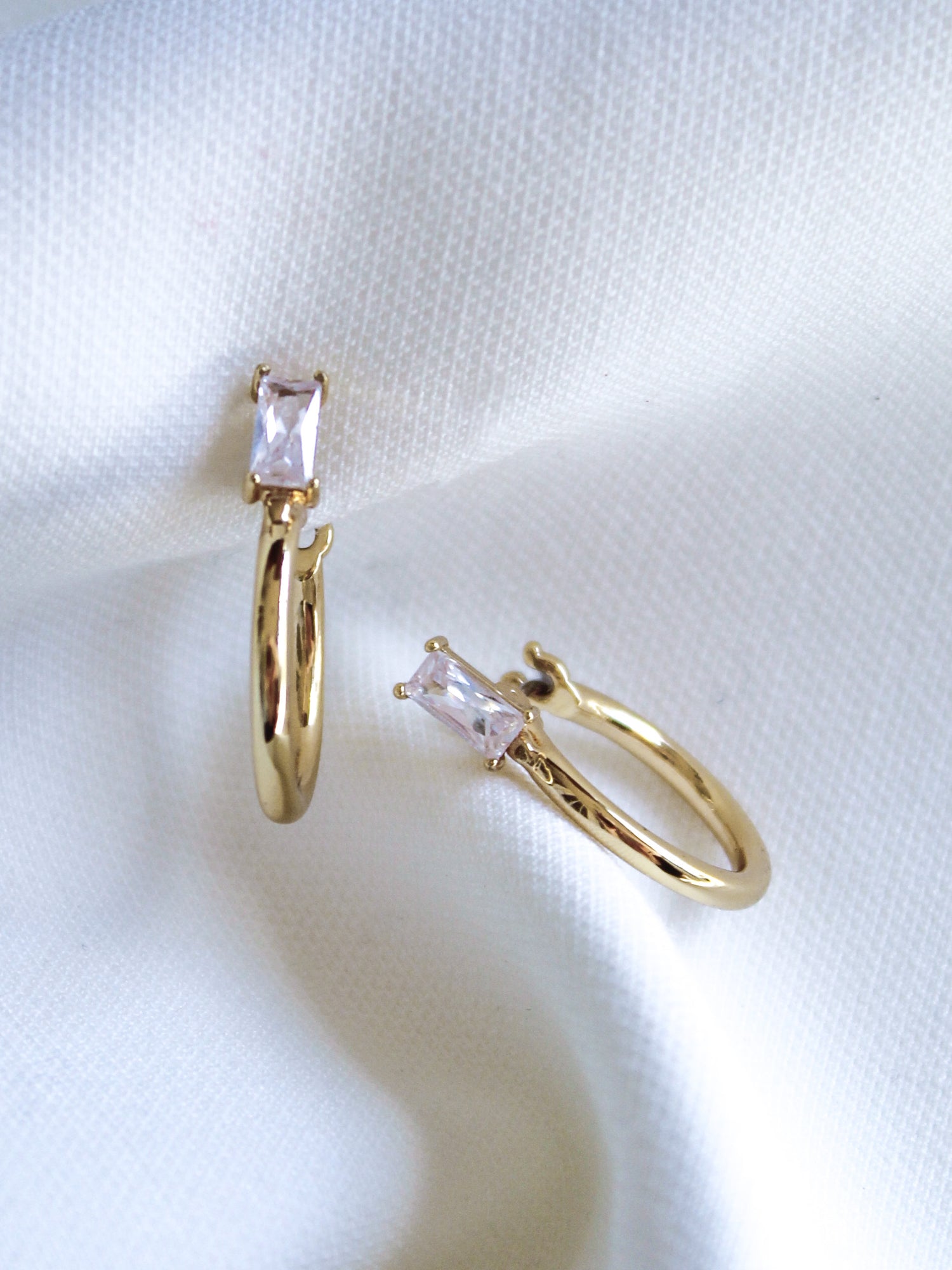 The Darra Hoop Mini by Kinsey Designs Archives are gold-plated hoops with a 0.75" diameter, featuring rectangular clear cubic zirconia stones displayed on soft white fabric.