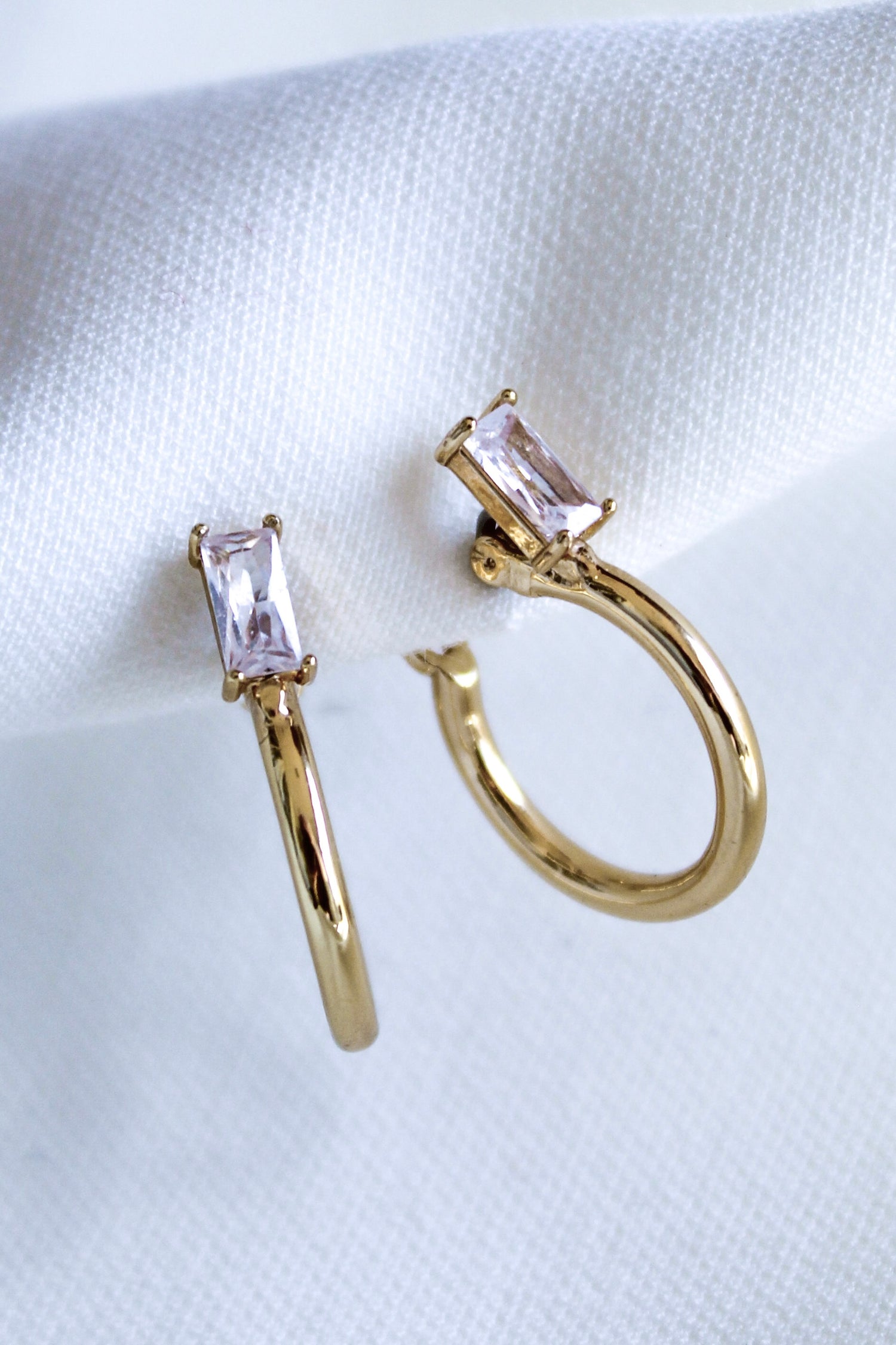 The Darra Hoop Mini by Kinsey Designs Archives are gold plated hoop earrings with a .75" diameter, adorned with rectangular clear cubic zirconia gemstones, displayed on a white fabric background.