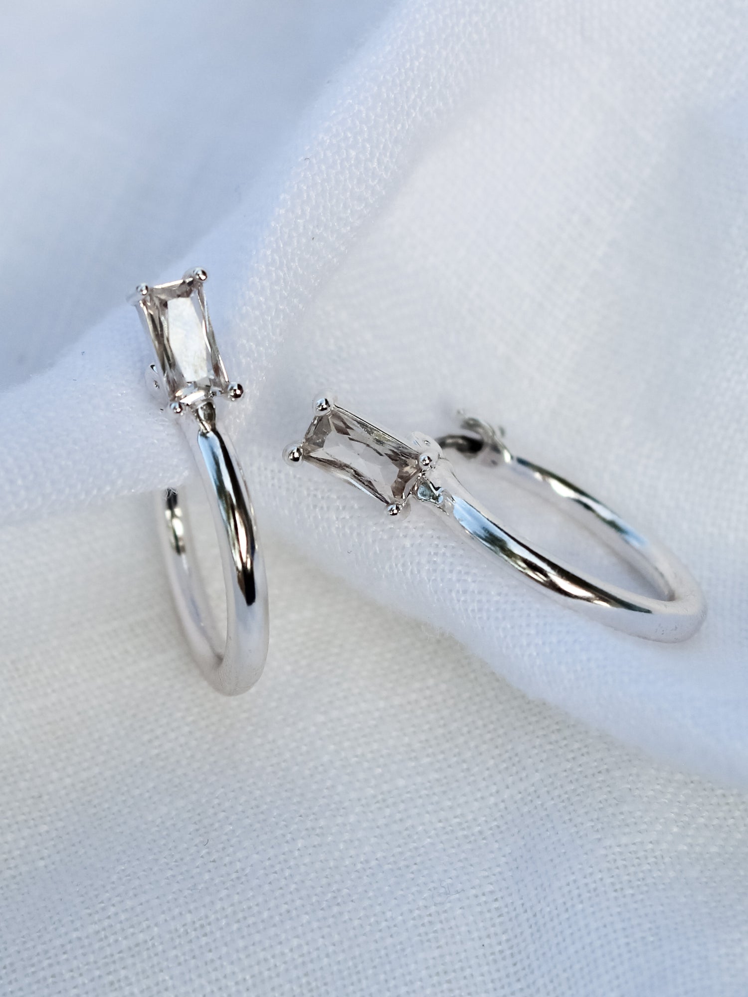 The Darra Mini Silver rings by Kinsey Designs Archives, crafted from rhodium plated brass with rectangular clear cubic zirconia, are displayed on white fabric.