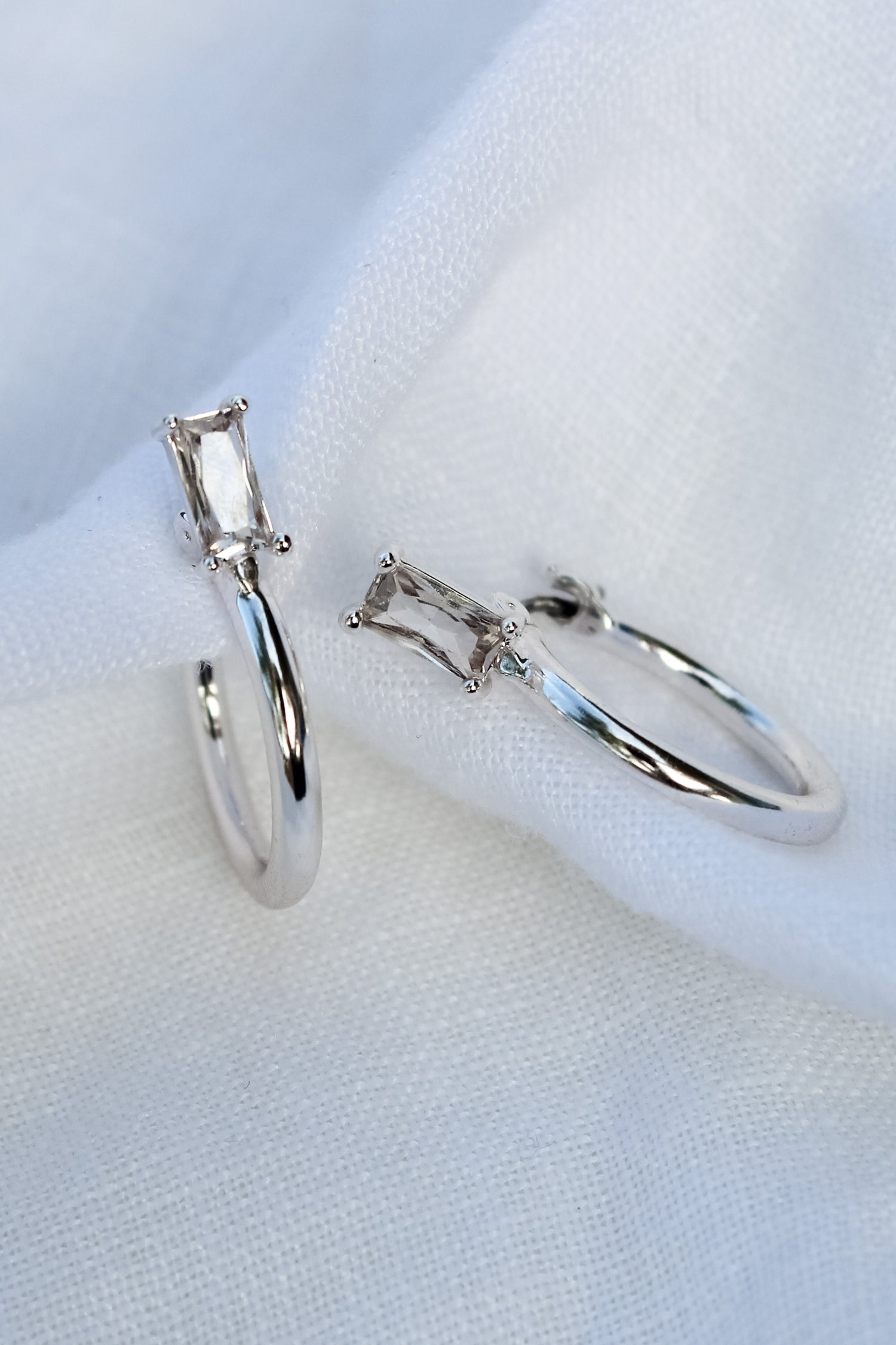 The Darra Mini Silver rings by Kinsey Designs Archives, crafted from rhodium plated brass with rectangular clear cubic zirconia, are displayed on white fabric.